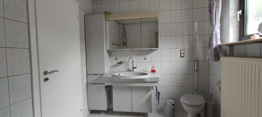 Helles Badezimmer mit Waschbecken, Toilette und Spiegel an der Wand.