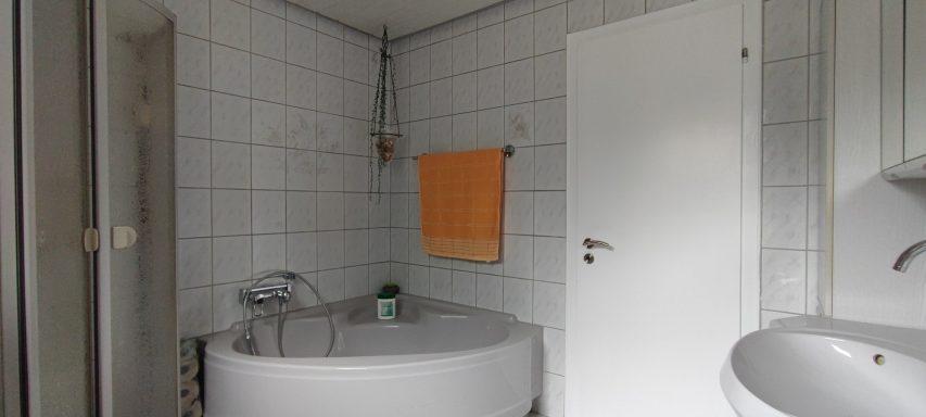 Helles Badezimmer mit Badewanne, Waschbecken und weißem Fliesenboden.